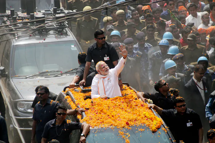Prime Minister Modo waving from a car driving down a busy street.