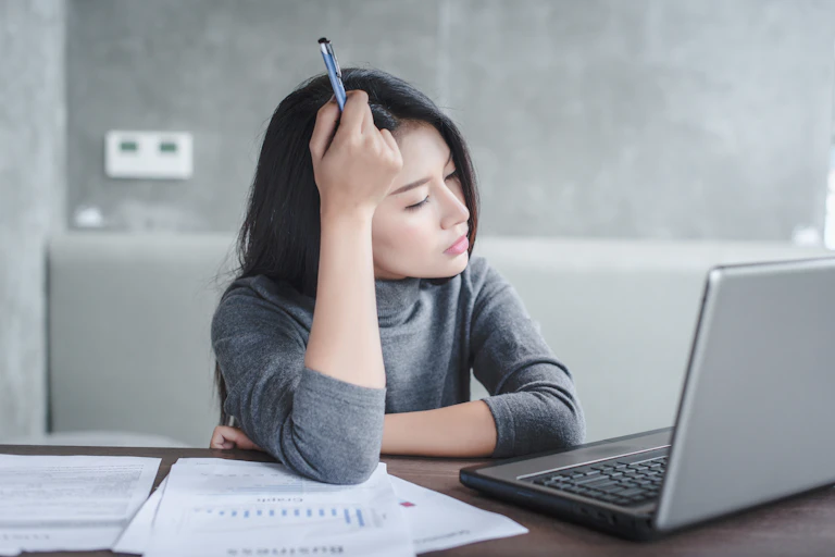 A young woman sits at a desk looking tired and exasperated