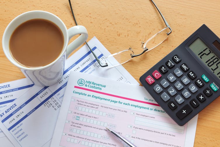 A cup of tea, HMRC tax forms, a pair of spectacles and a calculator arranged on a desk