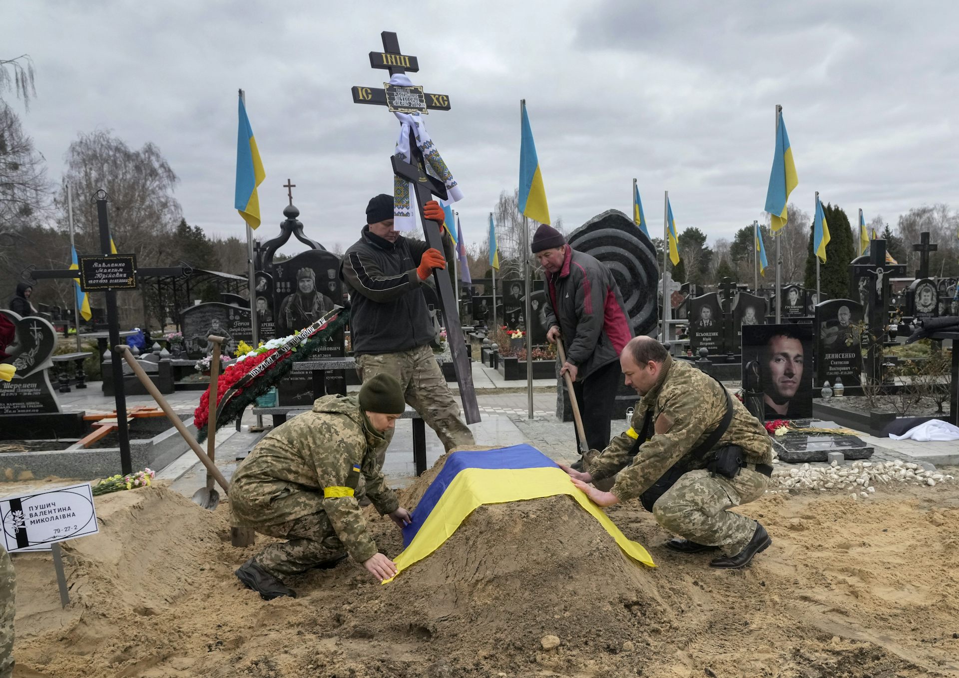 paramedics drape a ukrainian flag over a casket in a cemetery