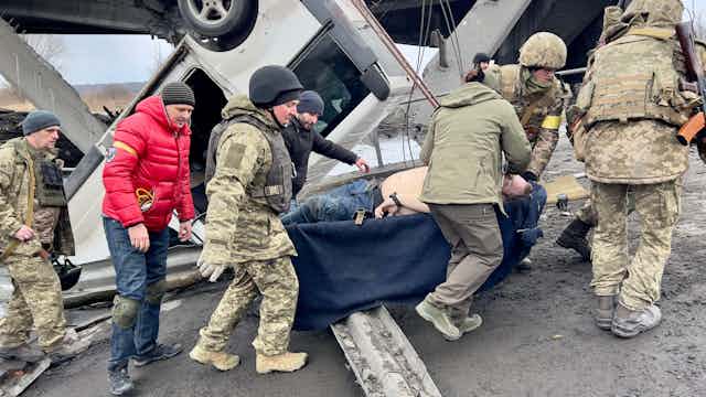 Armed Ukrainian soldiers evacuate an injured man after shelling Kyiv, Ukraine