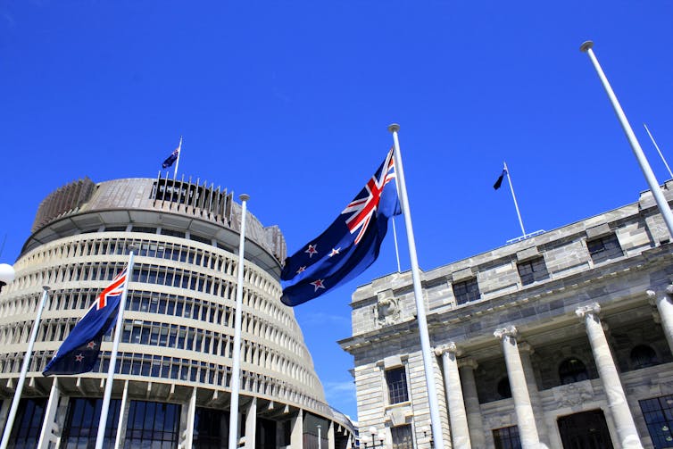 The outside of the New Zealand parliament building with national flags flying in front.