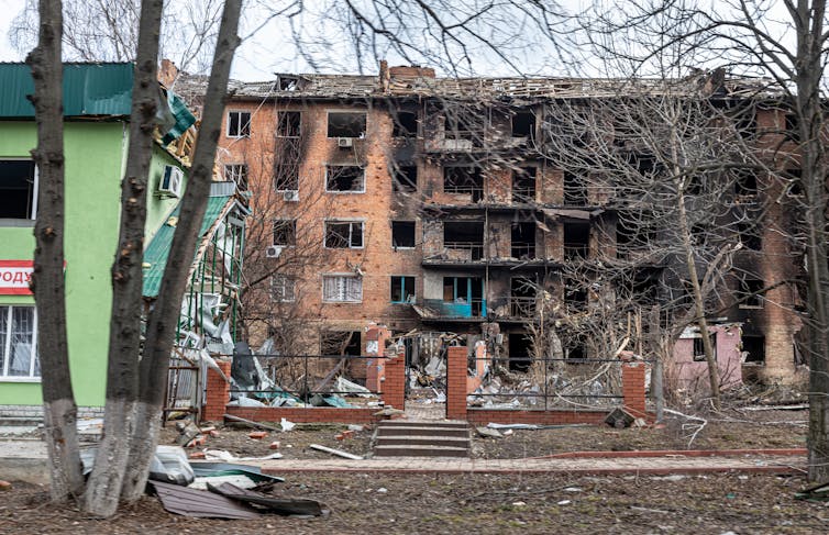 A destroyed multistory building, hit by bombs, with debris spread around it.