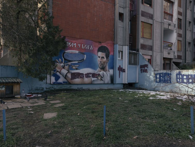 A mural on a building depicts a man with a tennis racket, with writing in Cyrillic script across the top.