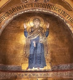 Mosaic seen of a woman with arms raised wearing long robes and a head covering.