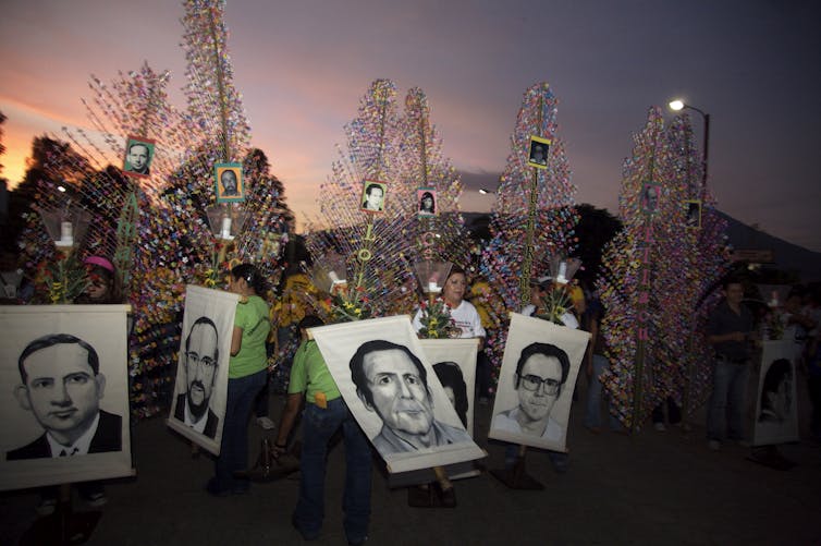 Dusk falls as protesters hold posters with black and white sketches of men's faces.