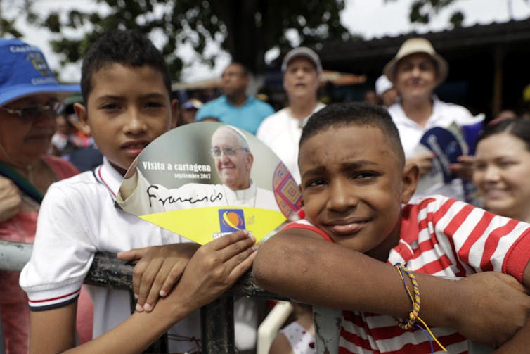 Two boys in a crowd hold a fan with a photo of Pope Francis.