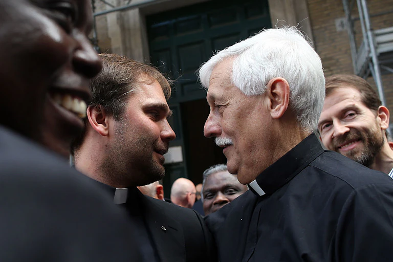 Two men wearing clerical collars talk in a crowd.