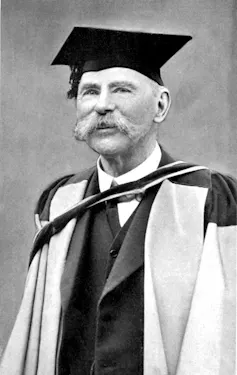A man in an academic gown and bushy moustache.