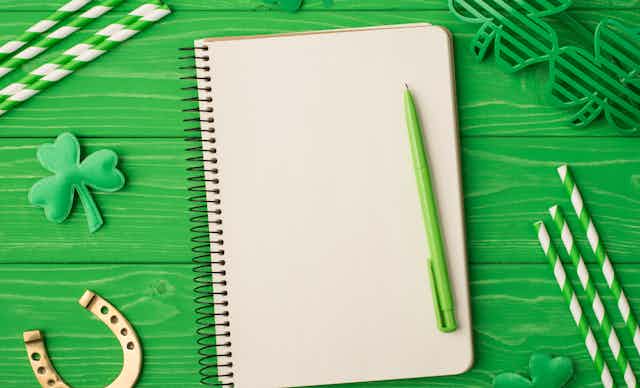 A blank notebook and green pen seen against a green table and shamrocks.