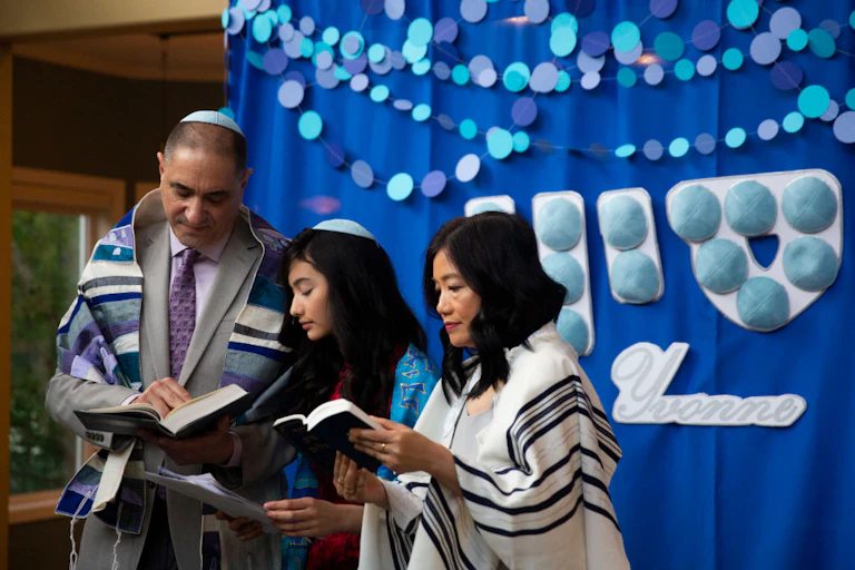A man and woman stand on either side of a girl wearing a yarmulke.