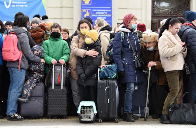 A crowd of people with suitcases, children wrapped in winter coats waiting on a train platform in Lviv
