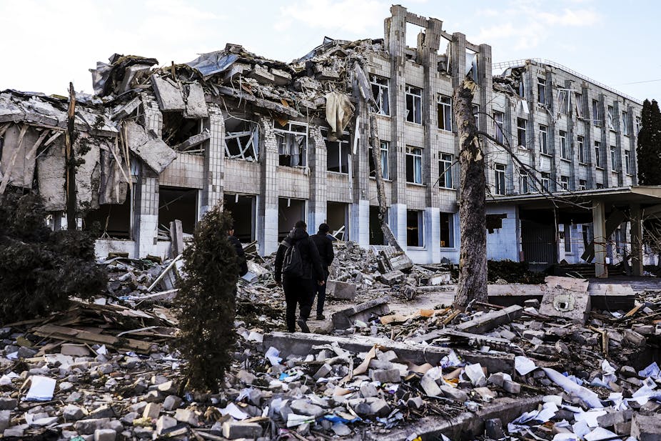 Two men walk on the rubble of a bombed four-storey school building