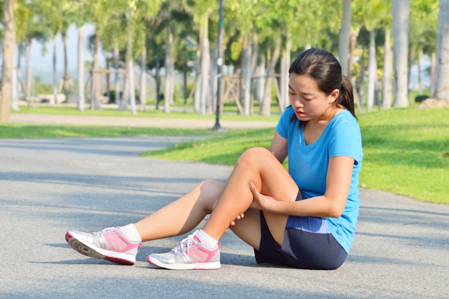 A young woman cradles her knee after suffering an injury while running.