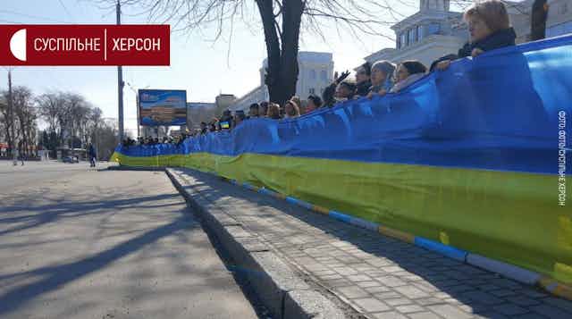 Men and women holding up a long banner with Ukrainian colours.
