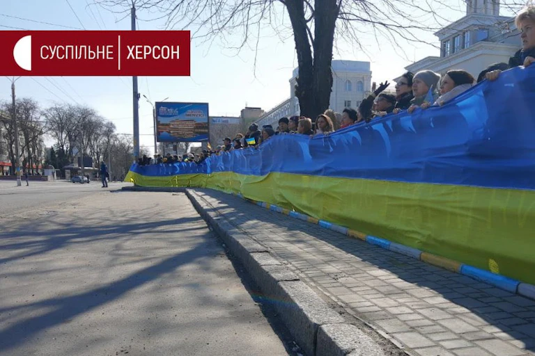 Men and women holding up a long banner with Ukrainian colours.