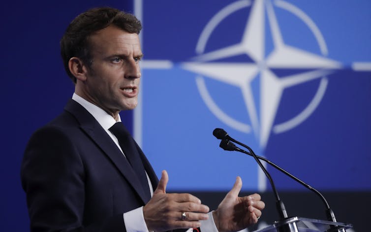 Emmanuel Macon giving a speech with a Nato logo in the background.