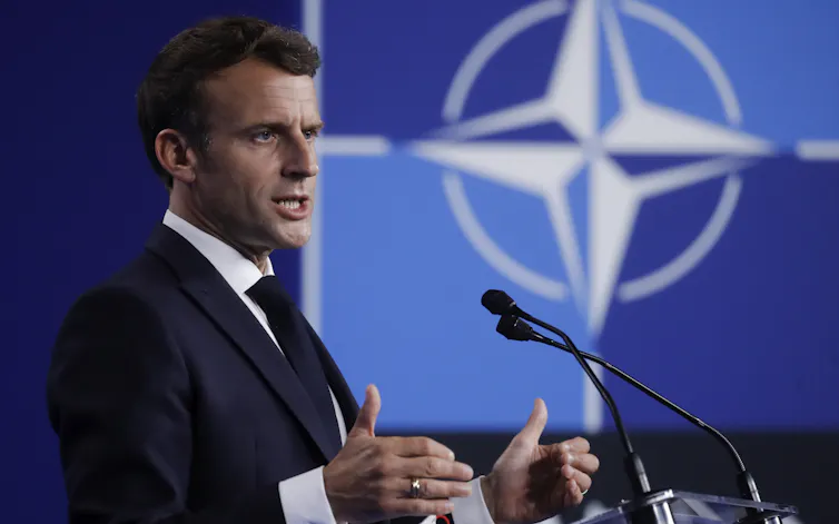Emmanuel Macon giving a speech with a Nato logo in the background.