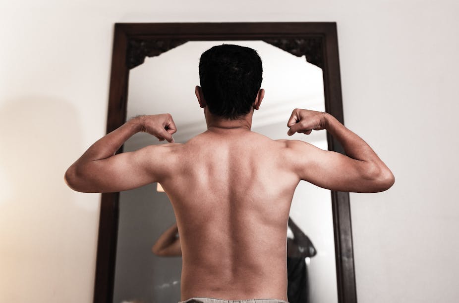 A man flexes his muscles in the mirror.