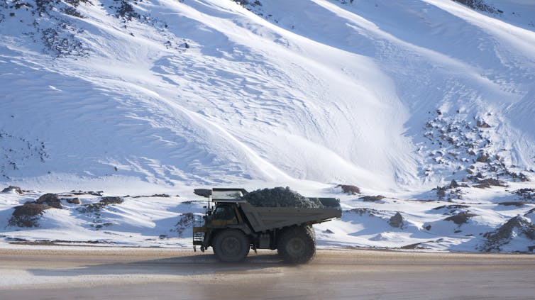 A dumper truck loaded with black ore on an empty road surrounded by snow.