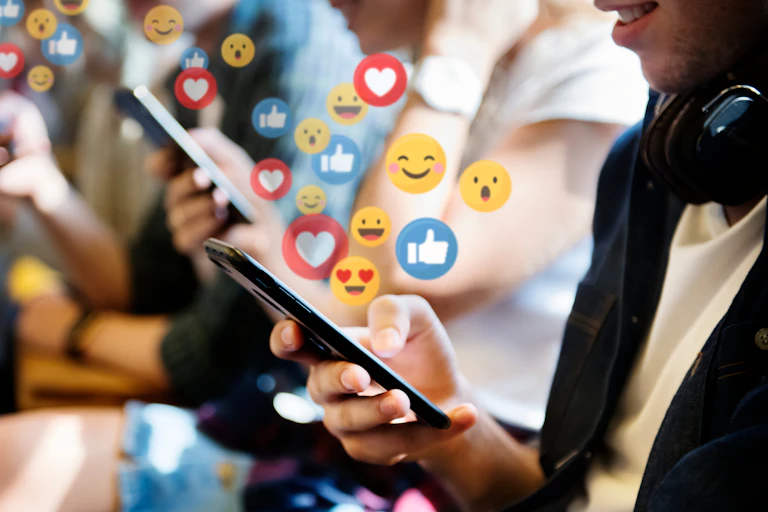 Close up of several hands holding mobile phones, with emoji icons emanating from the screens