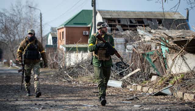 Armed men walk by wreckage.