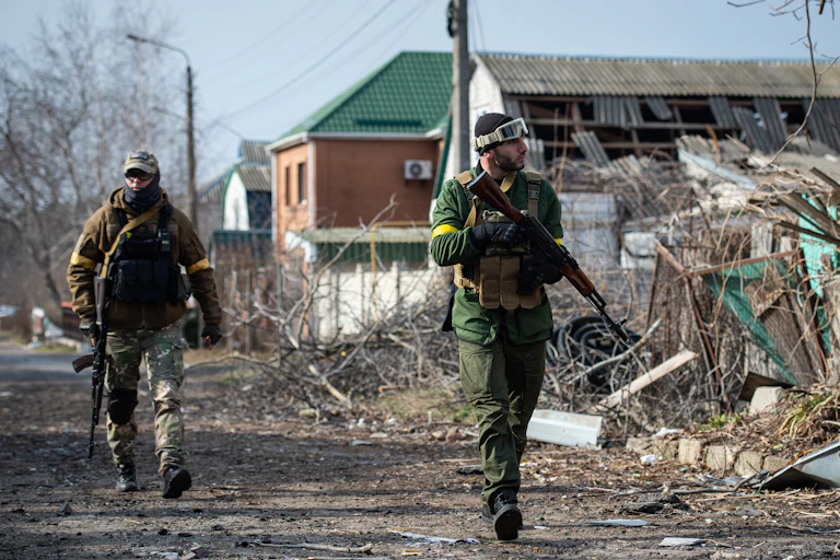 Armed men walk by wreckage.