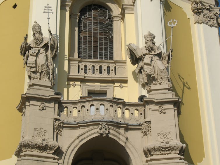 sculpture seen of a statue of a man on the side of a church wearing a bishop's hat and holding a staff