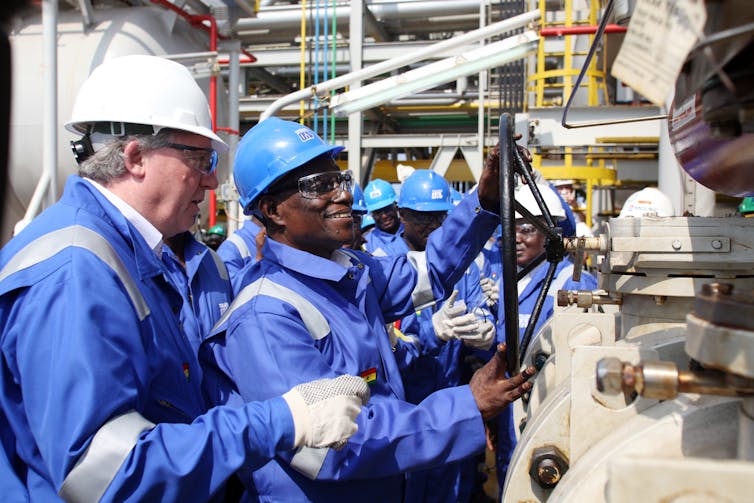 Men on an offshore oil platform in coveralls and helmets, smiling as Ghanaian President John Atta Mills turns a valve to symbolically open oil production in the Jubilee field off Ghana’s west coast, Dec. 15, 2010. Pius Utomi Ekpei/AFP via Getty Images)