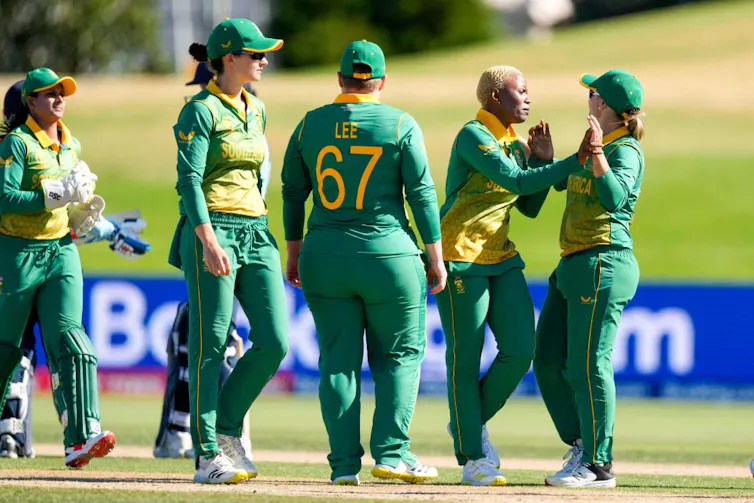 Ateam of women in green and gold outfits on a sports field, gathering together, two clasping hands.