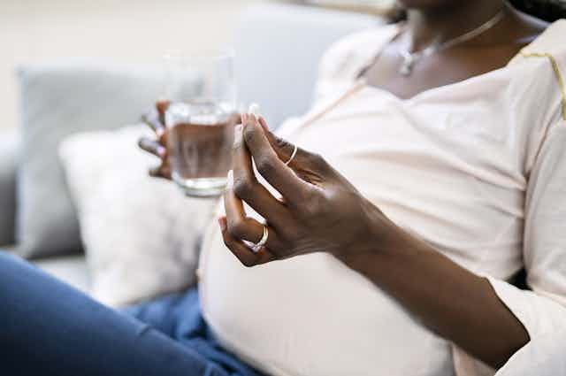 Photo d’une femme enceinte qui tient un cachet et un verre d’eau.