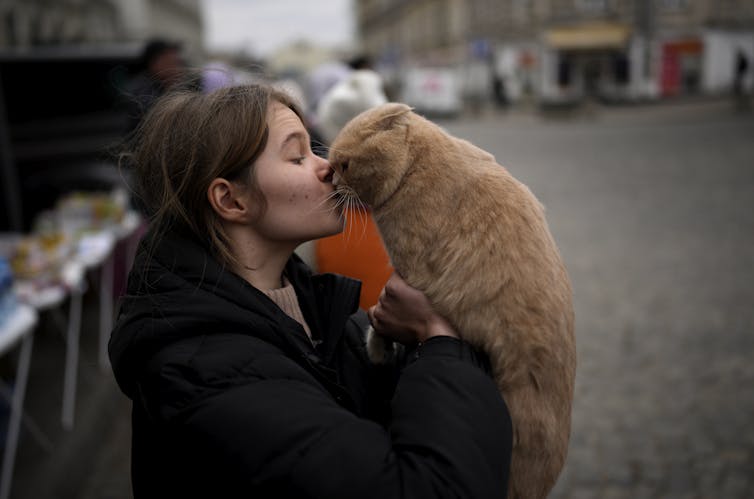 A woman kisses an orange cat.