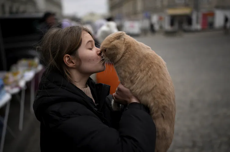 A woman kisses an orange cat.