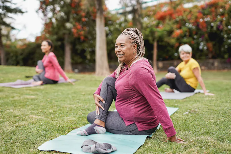 Three women on yoga mats on grass, stretching