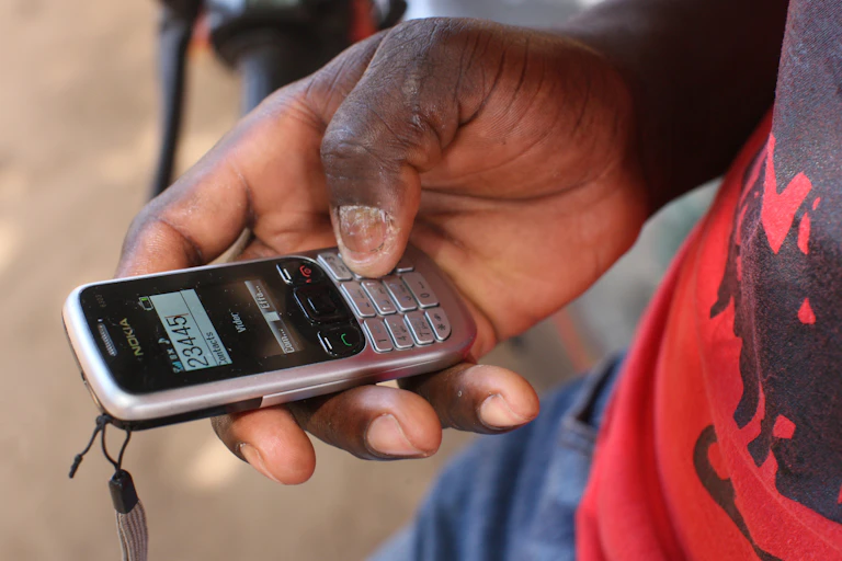 An African man holds a cel phone.