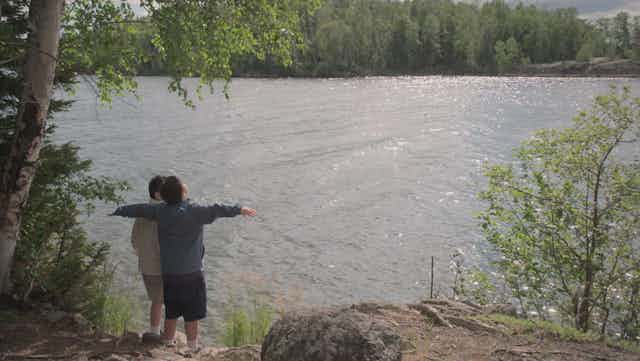Two young boys stand at the edge of a lake