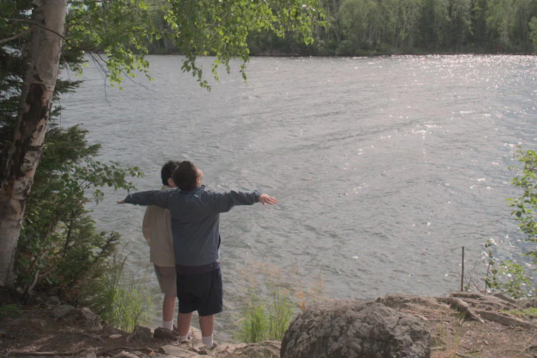 Two young boys stand at the edge of a lake