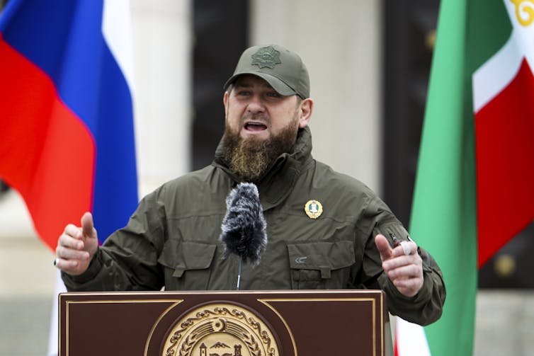Ramzan Kadyrov speaks, with flags in the background