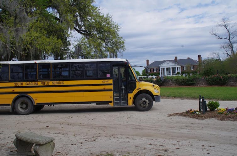A yellow school bus with South Carolina Public Schools printed on the side, a large house is in the background