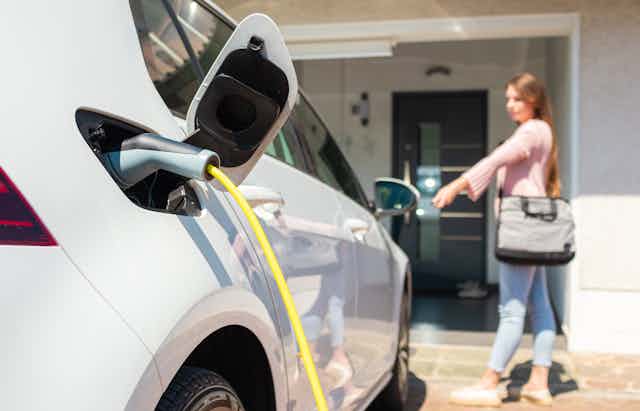 Electric car charging port with power lead plugged in and a woman standing in the background