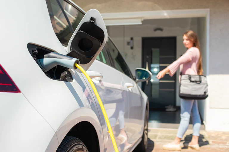 Electric car charging port with power lead plugged in and a woman standing in the background