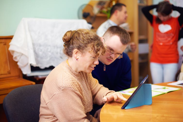 Man with disability looks at the tablet his disability services worker is showing him.