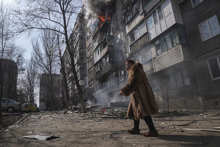 person walks past bomb-damaged apartment