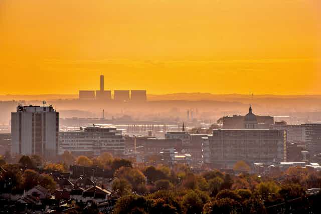 A cityscape against a yellow sky with a power station in the background.