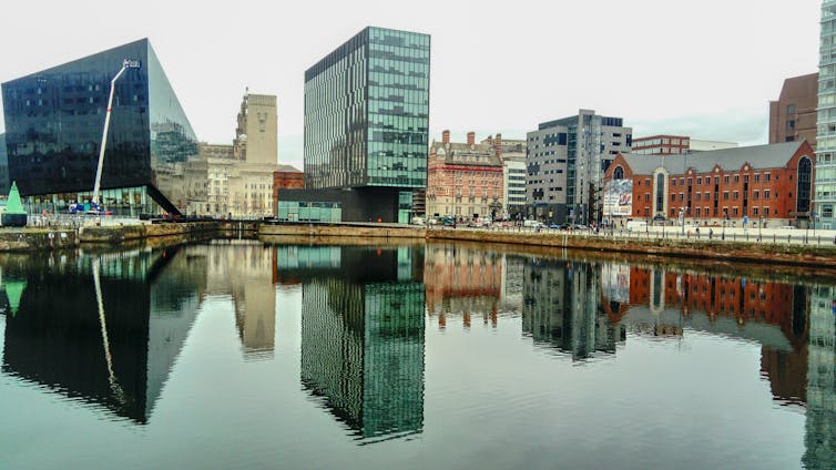 A view of a dock in a city, with tall glass buildings reflected in the water.