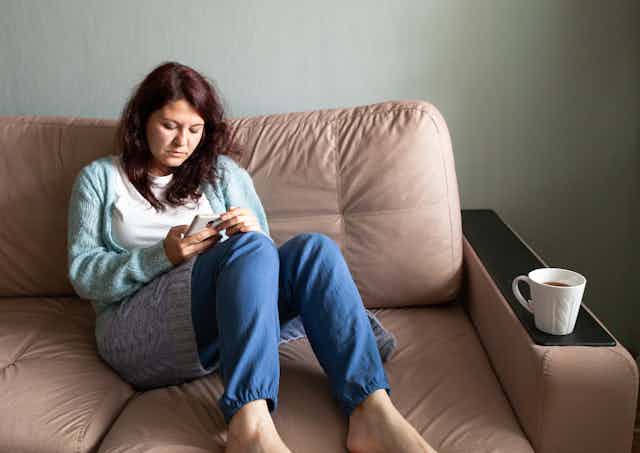 A woman sits on a couch looking at her phone.