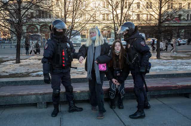 Two women being detained by armed Russian riot police.