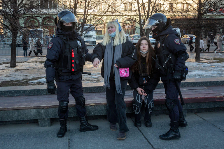 Two women being detained by armed Russian riot police.
