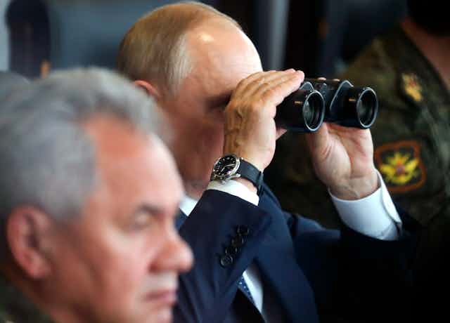 A bald man looks through binoculars.