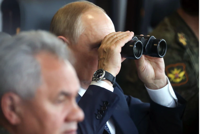 A bald man looks through binoculars.